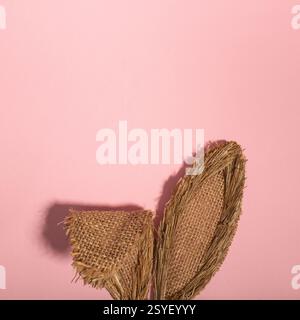 Orecchie coniglietto realizzate in materiale vegetale naturale su sfondo rosa pastello. Concetto minimalista di Pasqua. Posizione piatta. Foto Stock