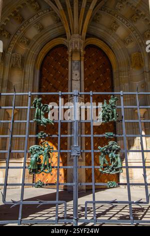 Un cancello in metallo dettagliato con sculture artistiche a rilievo in bronzo sorge di fronte ad un'entrata ornata in pietra ad arco con una grande porta in legno adornata Foto Stock