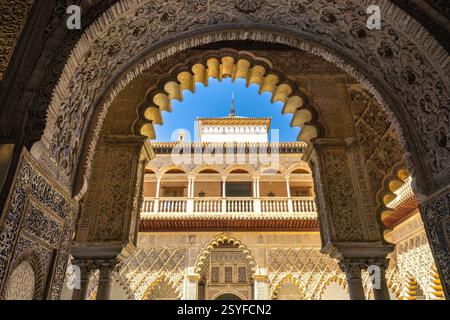 L'Alcázar di Siviglia, storico palazzo reale nella città di Siviglia, Andalusia, Spagna. Arcata decorata che incornicia un cortile del palazzo illuminato dal sole. Intricati lavori di pietra Foto Stock