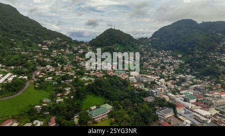 Densa zona residenziale annidata tra verdi colline con vegetazione lussureggiante, vari edifici e strade tortuose visibili. Seychelles, Mahe. Foto Stock