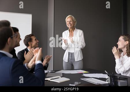 Una leader donna anziana applaude insieme al team dopo una collaborazione di successo Foto Stock