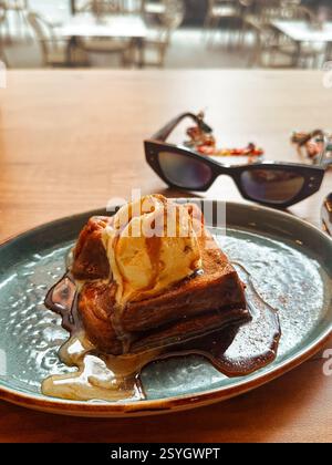 Madrid, Spagna 1° luglio 2024 Torrijas dessert tradizionale spagnolo con gelato, occhiali da sole neri da donna su un tavolo in un caffè. Delizioso dolce sul piatto. Foto Stock