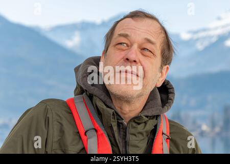 Un viaggiatore con uno zaino si erge davanti a vette innevate e a un lago riflettente Foto Stock
