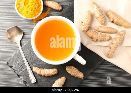 Tè aromatico alla curcuma, polvere e rizomi su tavolo nero, piatto Foto Stock