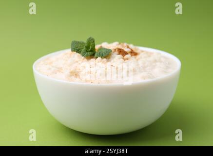 Gustoso budino di riso con cannella e menta nel recipiente su sfondo verde, primo piano Foto Stock