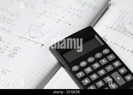 Copybook con formule matematiche scritte a mano e calcolatrice come sfondo, primo piano Foto Stock