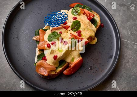 Gustoso sandwich a vista con salsa cremosa, salmone affumicato, spinaci freschi, semi di melograno vibranti su piatto scuro, piatto gourmet Foto Stock