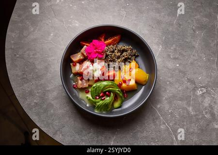 Vivace Poke Bowl con avocado, tonno, riso e fiori commestibili sulla superficie di pietra, che promuove il concetto di mangiare sano Foto Stock