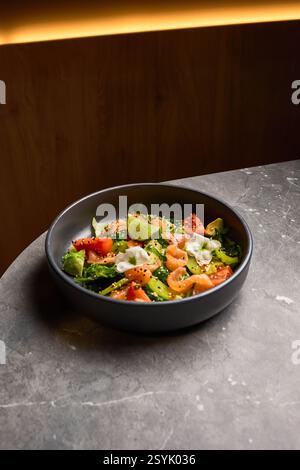 Insalata di avocado, pomodoro e salmone guarniti con lime in piatto nero su superficie in marmo, concetto di mangiare sano Foto Stock