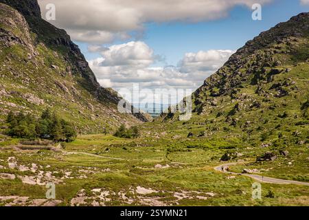 Una vista panoramica su una valle situata tra montagne verdeggianti sotto un cielo soleggiato, che mette in risalto la bellezza naturale e il fascino tranquillo. Foto Stock