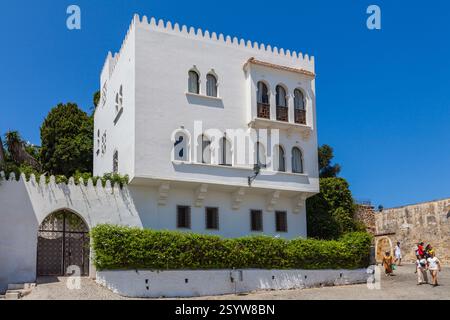 Edificio dipinto di bianco con uno stile architettonico distintivo, caratterizzato da finestre ad arco, un tetto piatto e un giardino circostante, che creano una pittoresca M Foto Stock