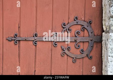 Una chiusura in metallo splendidamente realizzata adorna una porta in legno intemprata in un vecchio villaggio, mostrando un design intricato. Foto Stock