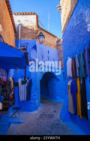 strada stretta e tortuosa in una città dipinta di blu, caratterizzata da edifici colorati, mostre di abbigliamento e un passaggio ad arco Foto Stock