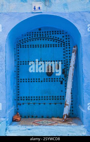 porta in legno ad arco blu vivace con borchie decorative e un battitoio, posta all'interno di una parete blu coordinata con una placca numerica sopra Foto Stock