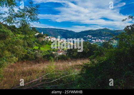 Una vista panoramica di una piccola cittadina annidata in una valle tra colline ondulate e vegetazione lussureggiante sotto un cielo blu Foto Stock