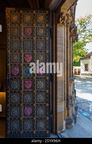 Una grande porta ornata con una griglia di pannelli decorativi con vari simboli e dettagli metallici, vista parzialmente aperta lateralmente, con architec Foto Stock