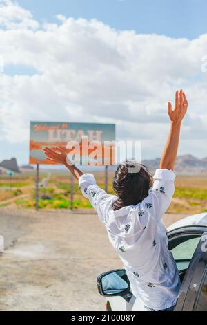 Bella donna nel suo viaggio vicino alla macchina. Benvenuto all'insegna dello Utah Road. Un grande cartello di benvenuto ti dà il benvenuto a Monument Valley, Utah Foto Stock