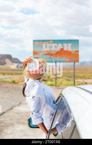 Bella donna nel suo viaggio vicino alla macchina. Benvenuto all'insegna dello Utah Road. Un grande cartello di benvenuto ti dà il benvenuto a Monument Valley, Utah Foto Stock