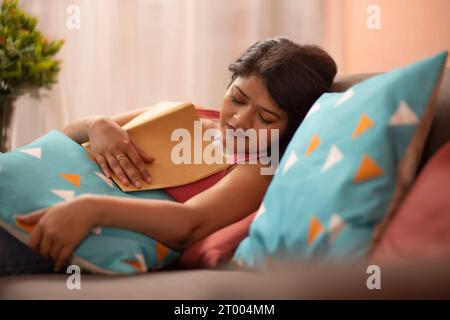 La giovane donna si addormenta mentre legge un libro in salotto Foto Stock