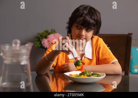 Ritratto di un ragazzo infelice che mangia broccoli Foto Stock