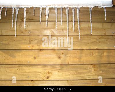 Ghiaccioli di fronte al muro di legno della capanna in Svizzera in inverno, icicle scintillante, spazio per cartoline di Natale testo, sfondo di legno per invito, cartellino Foto Stock