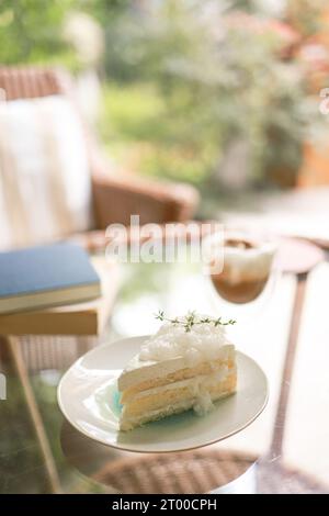 Torta al cocco e caffè in una caffetteria sullo sfondo sfocato. Dessert tradizionale a fette di deliziosa torta a strati di cocco Foto Stock