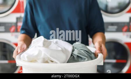 Marito della casa con cesto e vestiti sporchi lavati laundryÂ nell'interno della lavanderia. machineÂ lavatrice presso il negozio di lavanderia Foto Stock