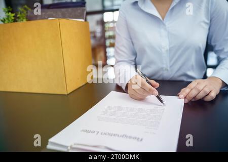 Donna d'affari che invia una lettera di dimissioni al capo e che tiene in mano le cose rassegnate deprimere o che porta una scatola di cartone alla scrivania in ufficio Foto Stock