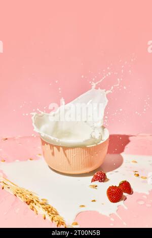 Dolce e sano. Ciotola con latte, cereali, muesli e frutti di bosco su sfondo rosa. Colazione salutare Foto Stock