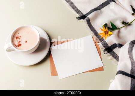 Una tazza di cappuccino speziato e carta bianca, quadri e fiori gialli su sfondo verde chiaro. Vista dall'alto, base piatta, mockup. Foto Stock