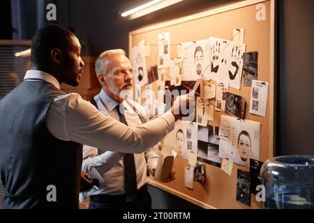 Ritratto laterale di un detective afroamericano che indica la bacheca delle prove mentre indaga sul caso Foto Stock