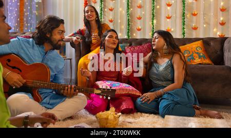 Amici che celebrano Diwali insieme a casa cantando Foto Stock