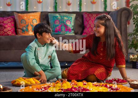 Fratello e sorella si divertono decorando il pavimento con fiori (Rangoli) in occasione di Diwali Foto Stock