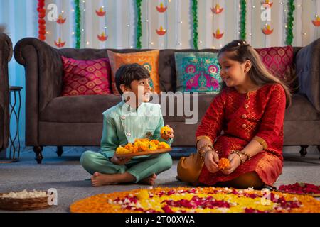 Fratello e sorella decorano il pavimento con fiori (Rangoli) in occasione di Diwali Foto Stock