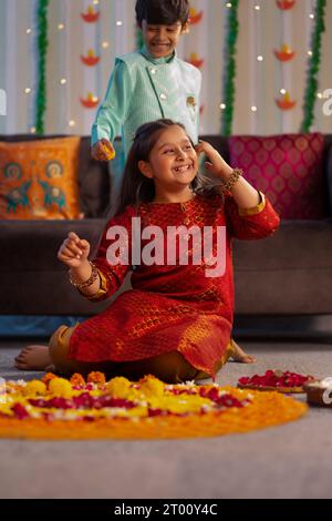 Ragazza che fa rangoli floreali in occasione di Diwali e ragazzo in piedi dietro Foto Stock