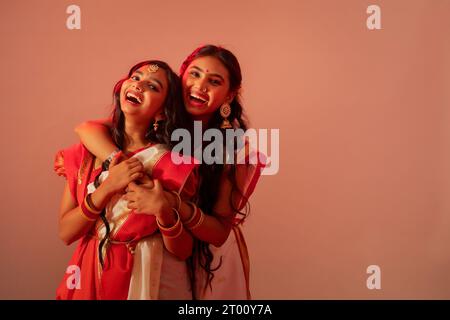 Due sorelle bengalesi in sari bianchi che si abbracciano su sfondo semplice Foto Stock