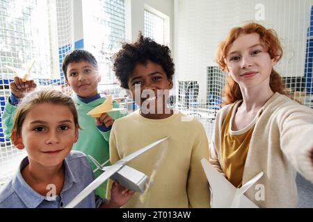 Gruppo di bambini che fanno selfie quando frequentano un corso di aeromodeling dopo la scuola Foto Stock