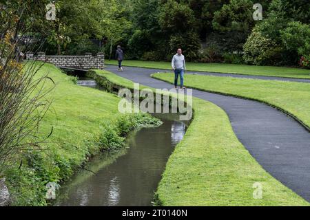 Persone che camminano lungo un sentiero vicino a un fiume che scorre attraverso i Trenance Gardens a Newquay, in Cornovaglia, nel Regno Unito. Foto Stock