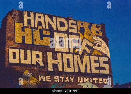 Enorme, attivista: Graffiti 'Hands of Our Homes' sul lato di un edificio domestico a Kopernicker Strasse, berlino, Germania. Mostra un certo attivismo e opposizione nella città verso la gentrificazione del vicinato e l'ascesa dei broker immobiliari che realizzano molti profitti. Immagine ripresa su una vecchia pellicola Kodak analogica. Foto Stock