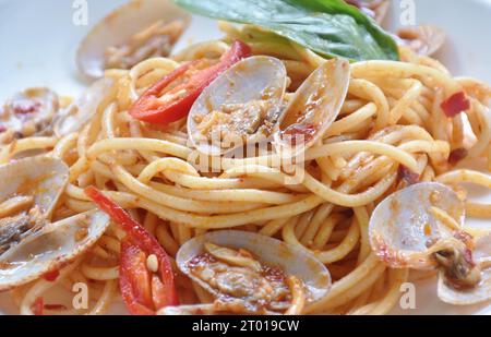 spaghetti speziati e fritti con peperoni e foglie di basilico sulla piastra Foto Stock