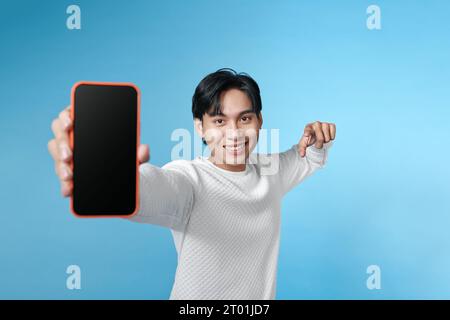 L'uomo sorridente tiene uno smartphone tra le mani e mostra il dito su uno schermo vuoto Foto Stock