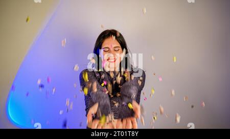 Allegra e bella bruna che soffiava i coriandoli dalle mani. Celebrazione della festa. Atmosfera festosa di Capodanno. Evento divertente. Conc. Natalizio Foto Stock