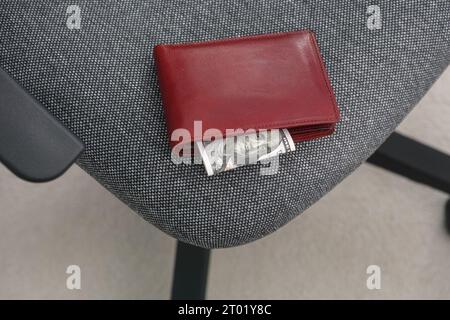 Un portafoglio con una banconota da cento dollari che ne esce sdraiato su una sedia da ufficio. Primo piano. Foto Stock