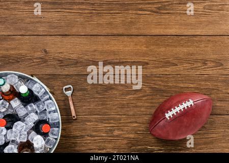 Guardando in basso un football americano seduto accanto a una vasca galvanizzata con bottiglie di birra assortite, seduto su un vecchio tavolo di legno con un apribottiglie. Foto Stock