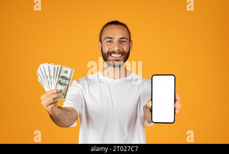 Un ragazzo europeo adulto sorridente mostra lo smartphone con uno schermo vuoto e un sacco di soldi Foto Stock