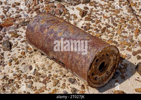 Un ampio filtro dell'olio per auto arrugginito lungo con fori che si aprono su una vista ravvicinata del terreno sabbioso in una giornata di sole Foto Stock