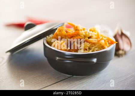 Classico pilaf cotto con carne, uvetta, aglio e altri ingredienti in una ciotola su un tavolo di legno. Foto Stock