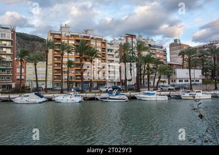 Cullera, Spagna - 8 gennaio 2023 - Vista sul fiume Jucar con edifici residenziali, barche e palme nella città di Cullera in Spagna Foto Stock