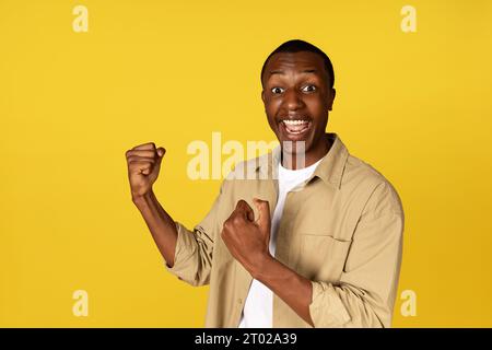 Felice uomo afro-americano millenario con la bocca aperta, solleva pugni, urla, celebra la vittoria Foto Stock