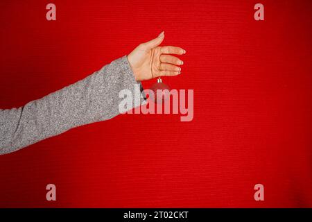 Pallina rossa circolare sull'albero di Natale in mano femminile isolata su sfondo rosso. La mano di una donna tiene un giocattolo decorativo dell'albero di Natale. Capodanno e Natale Foto Stock